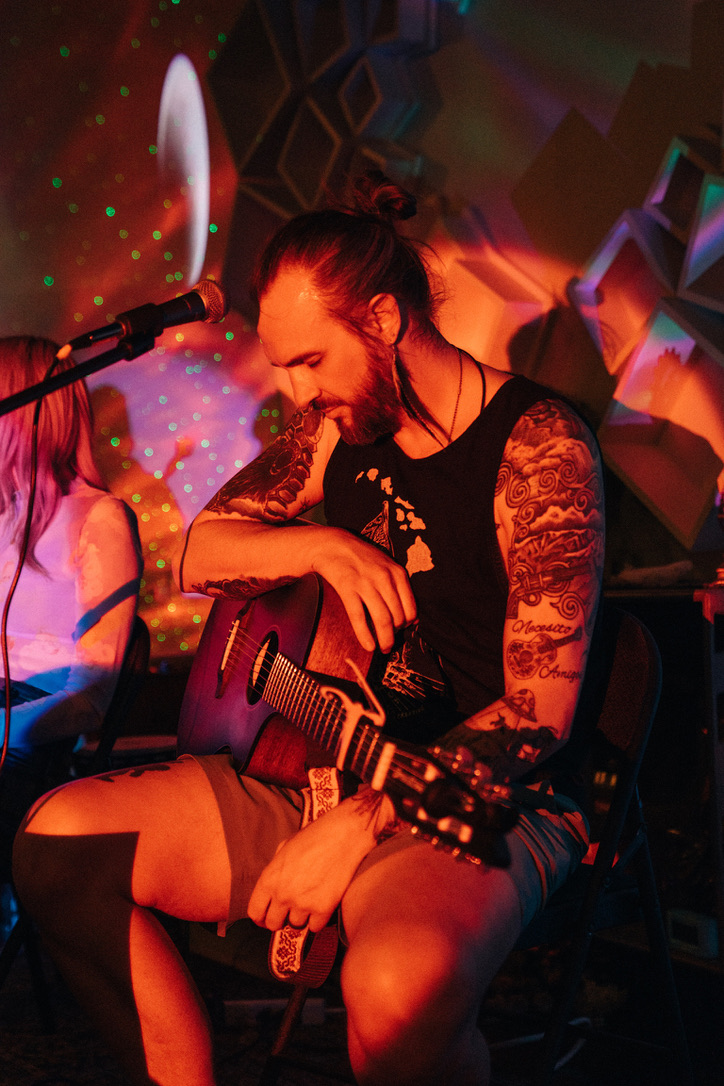Doug seated with an acoustic guitar under red light