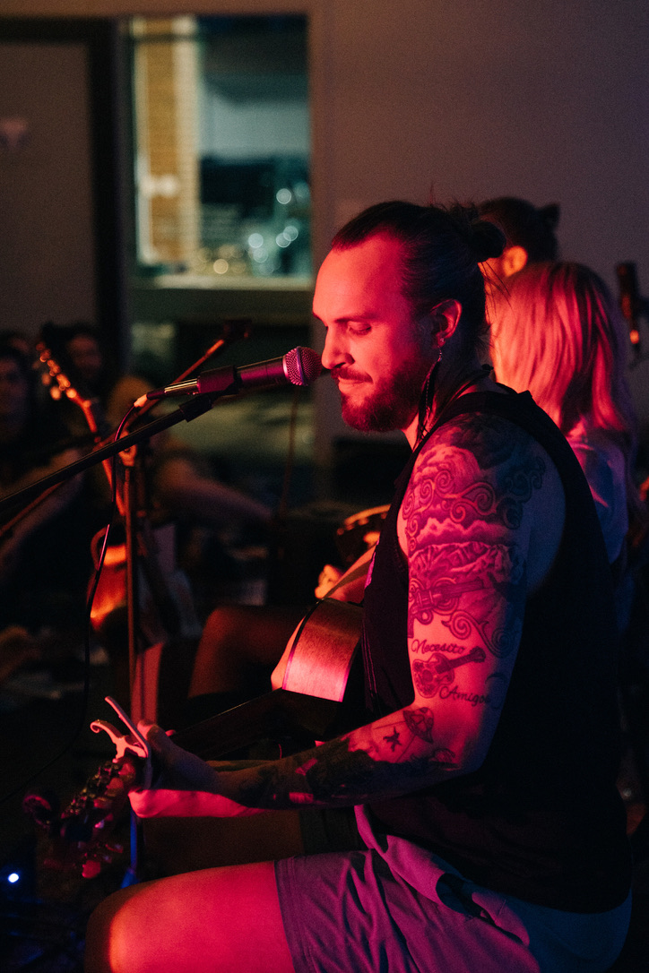 Doug singing and playing guitar under pink light