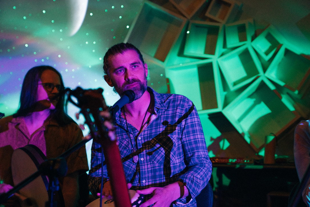 Michael with a hand drum, another musician beside him, under green light