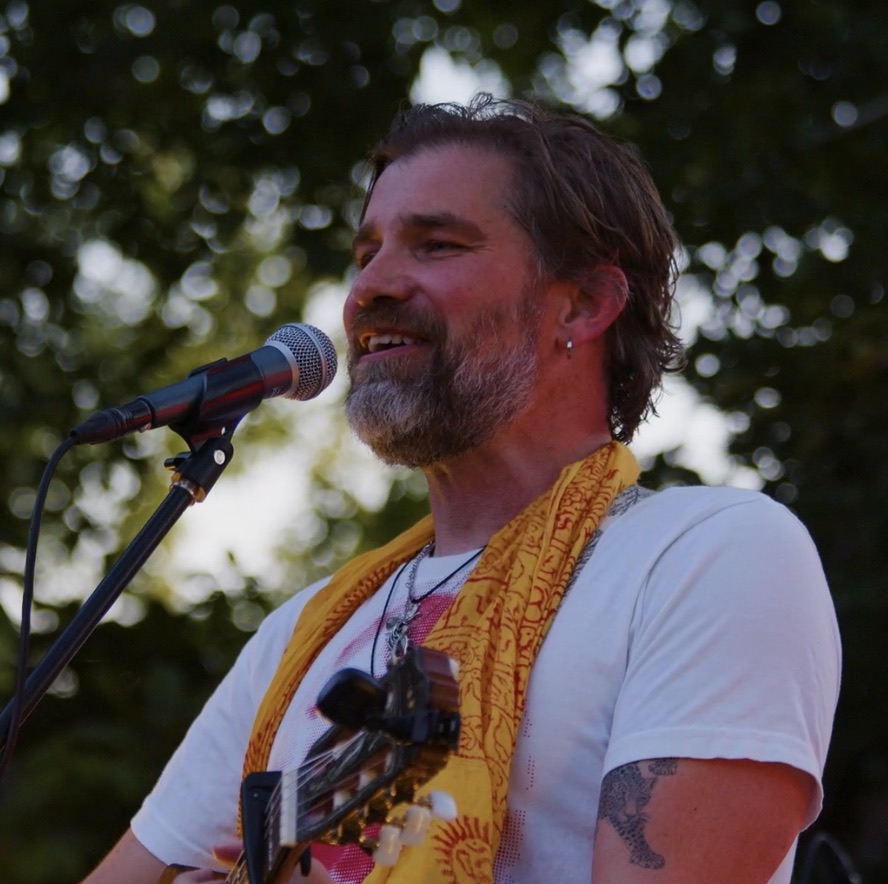 Michael singing at an outdoor show, yellow scarf, classical guitar